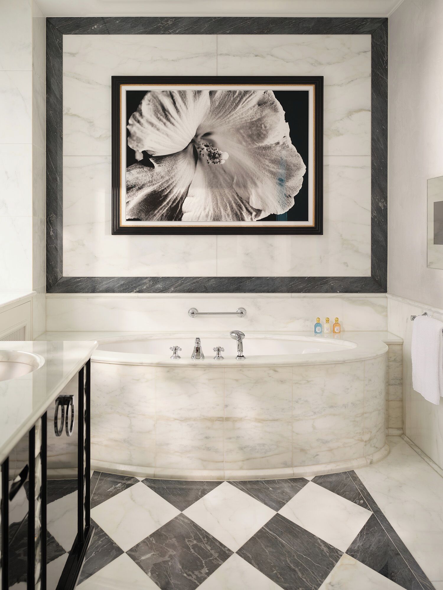 A modern bathroom with a large bathtub, a framed floral artwork on the wall, and a checkered floor pattern.