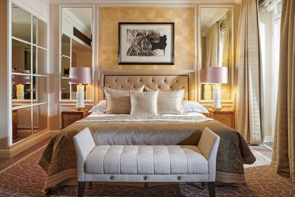 A luxurious bedroom with a large bed, a bench, and a mirror.