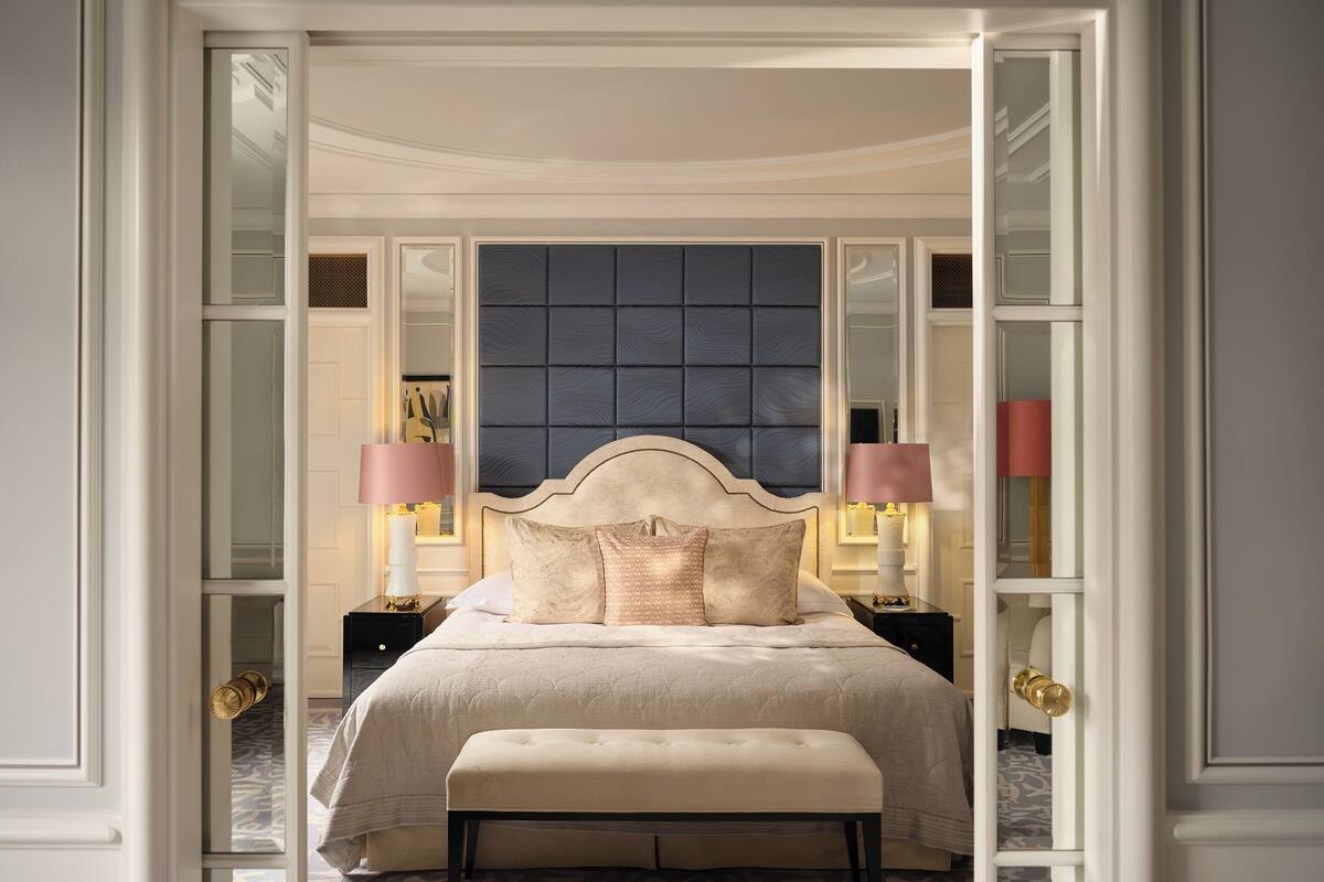 A bedroom with a large bed, two bedside tables with lamps, a bench, and a patterned carpet.