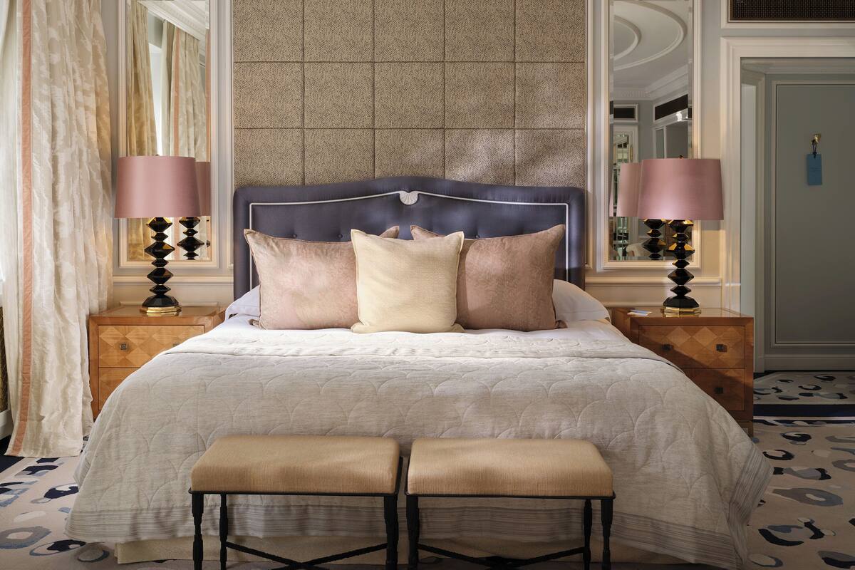 A neatly made bed with a headboard, two bedside tables with lamps, and a bench at the foot of the bed.