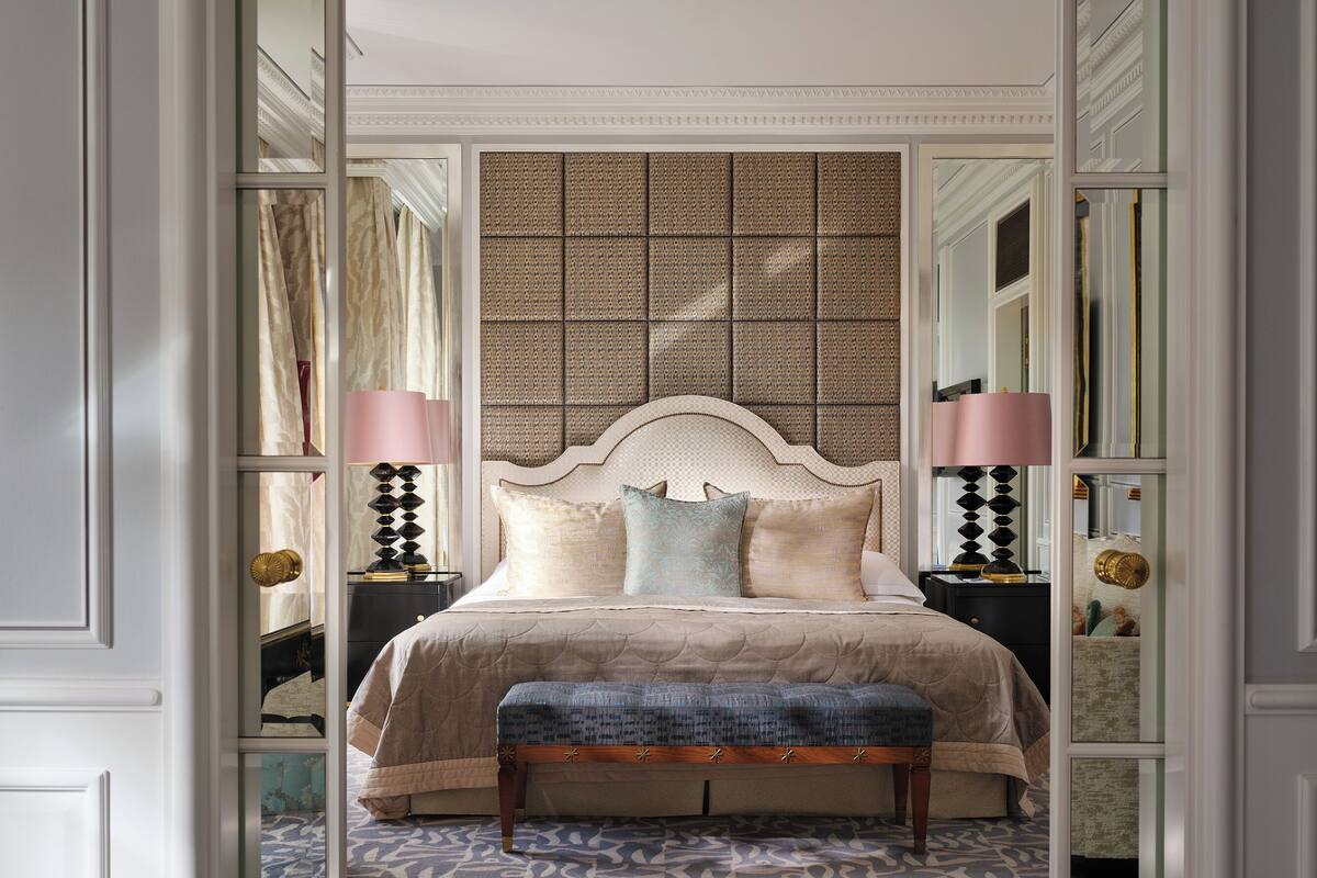 A bedroom with a large bed, two bedside tables with lamps, a bench, patterned carpet, and a decorative wall panel.