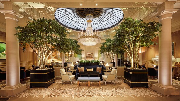 Un lobby espacioso con techo alto, una gran lámpara de cristal y columnas simétricas.