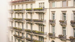Un edificio de varios pisos con balcones decorados con flores, un río al frente y un estilo arquitectónico clásico.