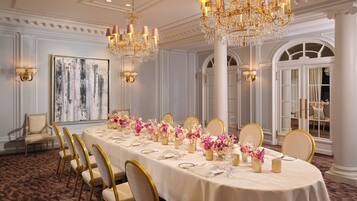 A formal dining room with a long table set for a meal, surrounded by chairs, and adorned with floral centerpieces.