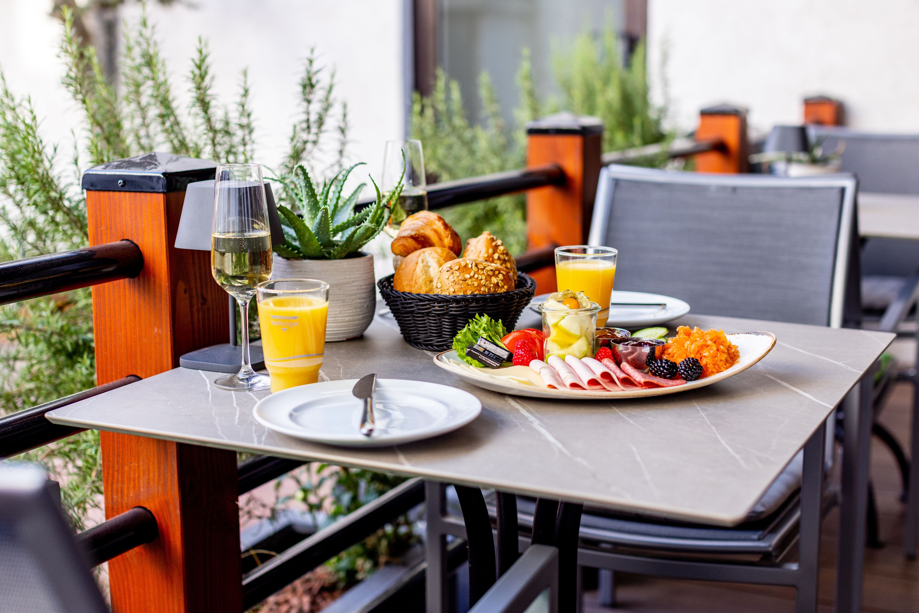 A breakfast table with croissants, fruit, and juice on a terrace with a view of greenery.