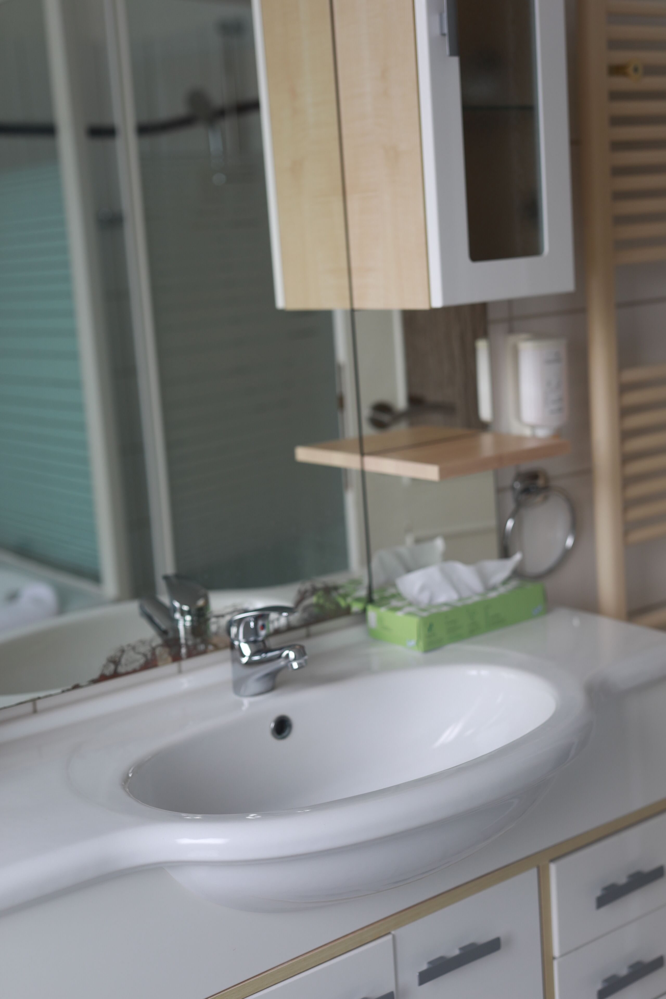 Un baño con un lavamanos blanco, un espejo y un armario de madera encima.