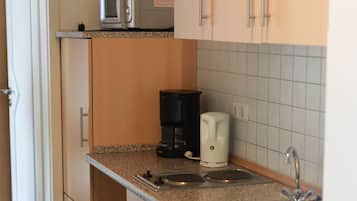 Eine kleine Küche mit Holzausstattung, einer Mikrowelle, einer Kaffeemaschine und einem Spülbecken.