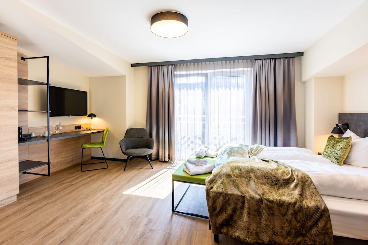 A modern hotel room with a bed, a desk, a chair, and a TV.