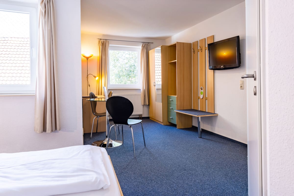 A hotel room with a bed, a desk, a chair, a TV, and a wardrobe.
