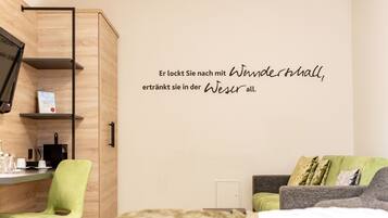 A modern hotel room with a bed, a green chair, a grey sofa, and a wall-mounted shelf with a book.