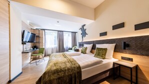 A modern hotel room with a large bed, a desk with a flat-screen TV, a chair, and a window with curtains. - Hotel zur Börse (Hamelin)