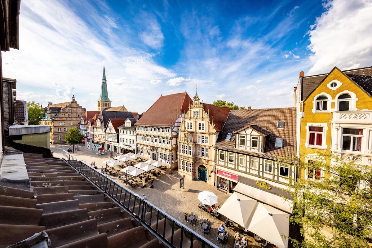 A town square with traditional buildings, outdoor seating, and a church spire.