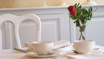 Une table dressée avec des tasses et des soucoupes blanches, ainsi qu’un vase contenant une rose rouge.