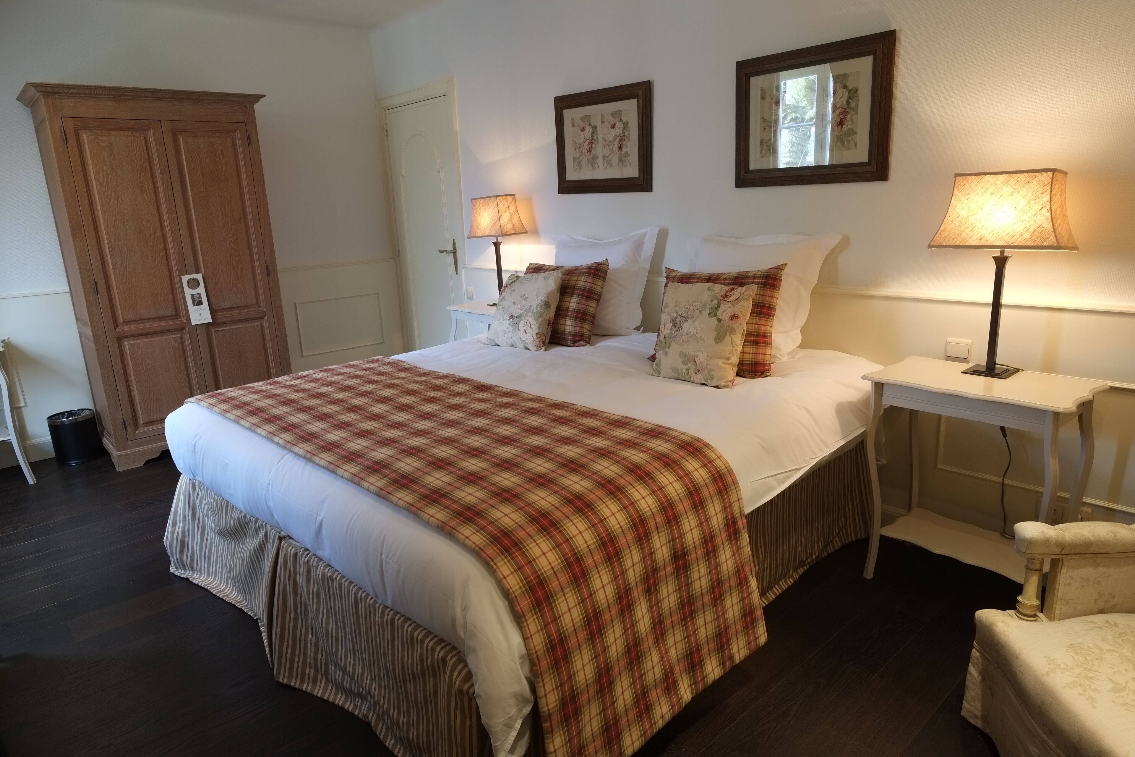 Cama bem arrumada com colcha xadrez, duas luminárias de cabeceira, mesa de cabeceira e guarda-roupa.