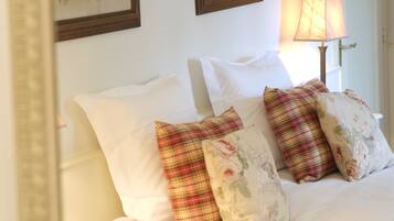 Een bed met witte beddengoed en meerdere kussens, waaronder bloemen- en geruite motieven.