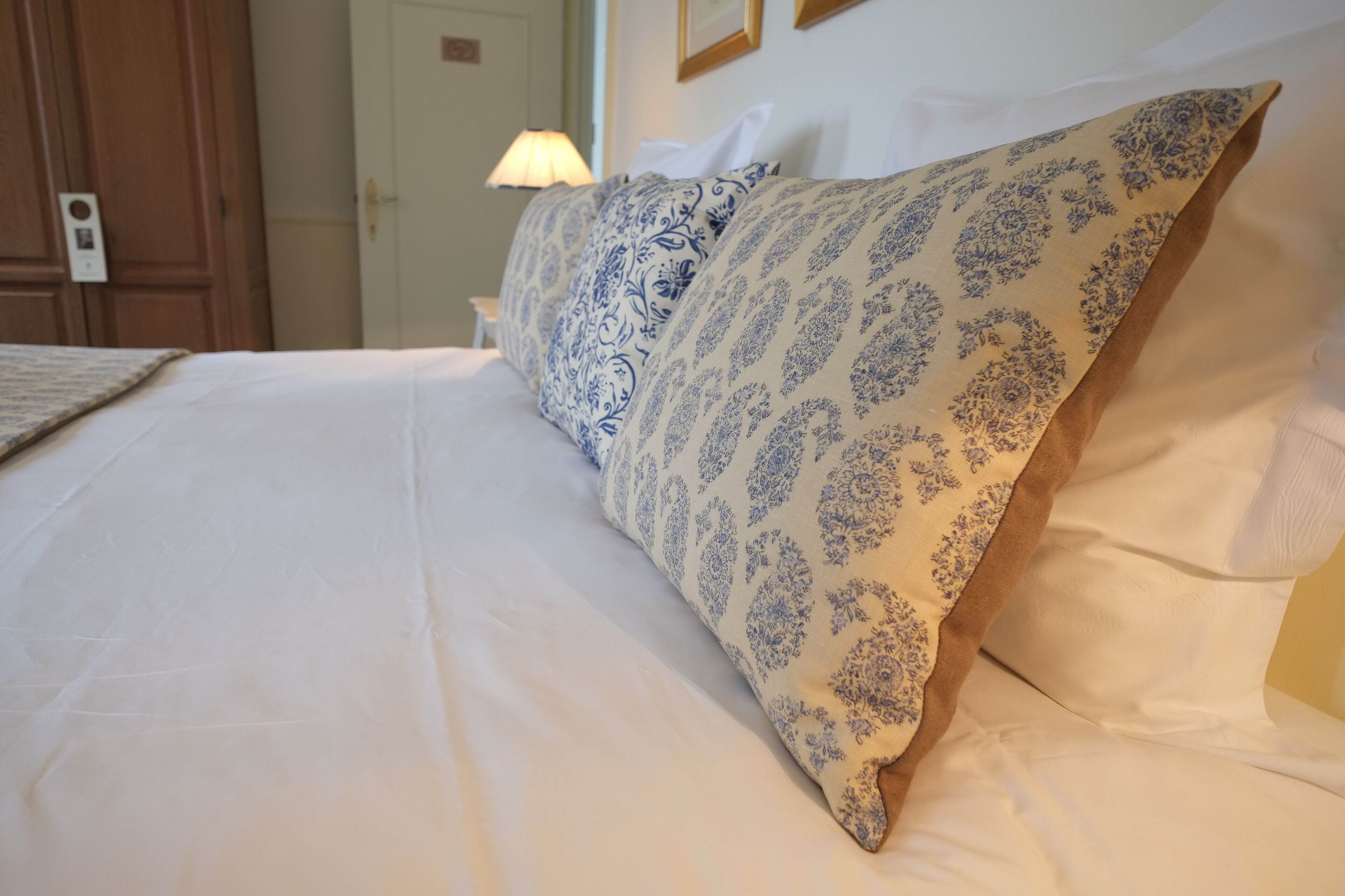 Een net opgemaakt bed met witte lakens en kussens met een blauw patroon.