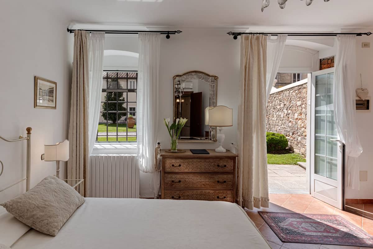 A bedroom with a bed, a dresser, a mirror, and a window with curtains.