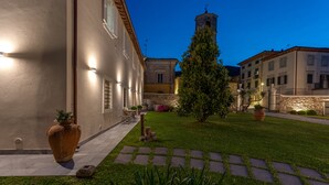 A courtyard with a well-maintained lawn, stone pathway, and a tall clock tower in the background. - Villa Del Papa (Lucca)
