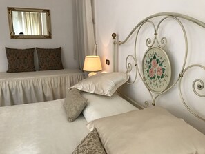 A bedroom with two beds, a bedside table with a lamp, a mirror, and floral-patterned pillows. - Villa Del Papa (Lucca)
