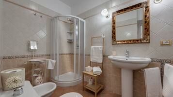 Un baño con ducha envuelta en cristal, lavamanos, inodoro y tocador con espejo.