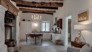 A spacious living room with a fireplace, a dining area with a wooden table, and a kitchen with white cabinets and a hanging light fixture. - Villa Del Papa (Lucca)