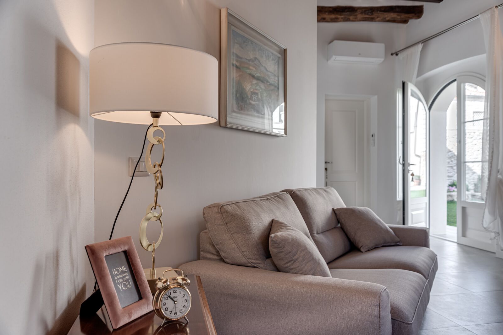 Ett vardagsrum med en soffa, en lampa, en klocka och en inramad tavla på ett sidobord.