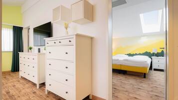 Habitación de hotel con cama, cómoda blanca, televisor y pared con un mural de paisaje montañoso.