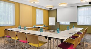 Une salle de conférence équipée d’une longue table, de chaises, d’un écran de projection et d’un tableau blanc.