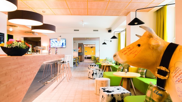 A modern interior with a reception area, bar, seating with cow-shaped stools, and a large cow decoration. - Hey Lou Hotel Piding (Piding)