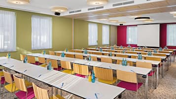 Une salle de conférence avec des rangées de tables, des chaises et un écran de projection.