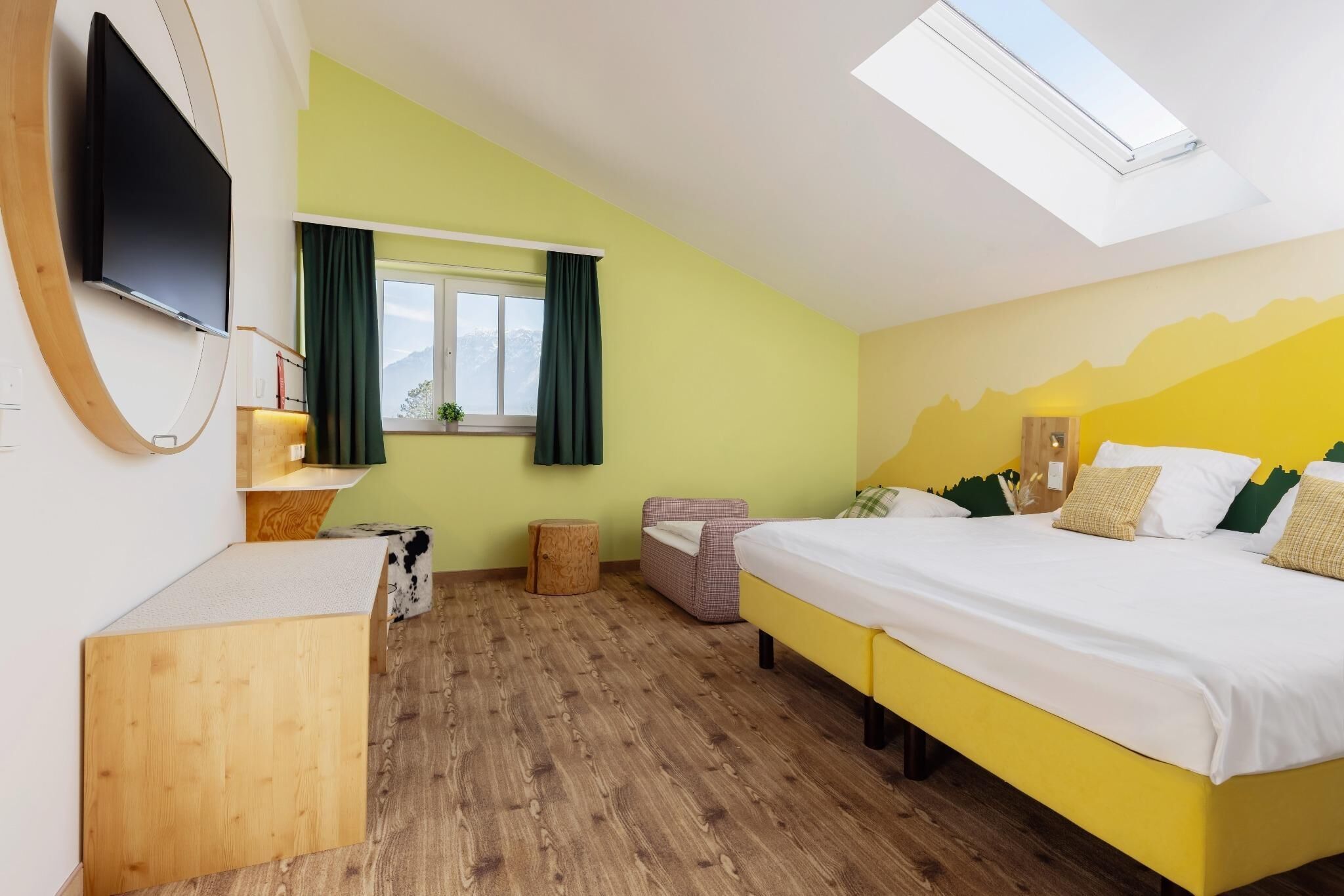 Ein Schlafzimmer mit einem Bett, einem Fernseher, einem Fenster mit Vorhängen, einem kleinen Hocker und einem Holztisch.
