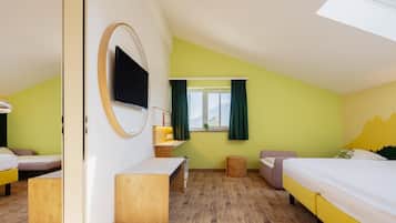 Ein Zimmer mit zwei Betten, einem Schreibtisch, einem Spiegel, einem Fernseher und einem Fenster mit Vorhängen.