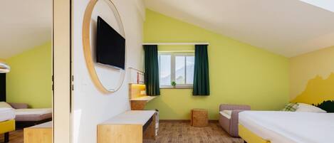 Ein Zimmer mit zwei Betten, einem Schreibtisch, einem Spiegel, einem Fernseher und einem Fenster mit Vorhängen.