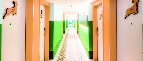 A hotel corridor with green and white walls, numbered doors, and a patterned floor.