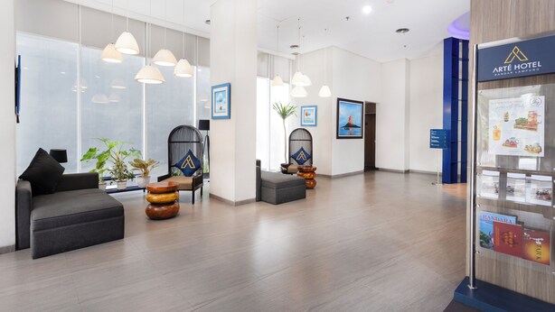 A modern hotel lobby with a reception desk, seating area, and a display of local attractions.