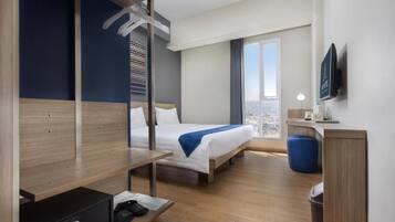 Habitación de hotel con cama, escritorio, silla, televisor y vista a la ciudad.