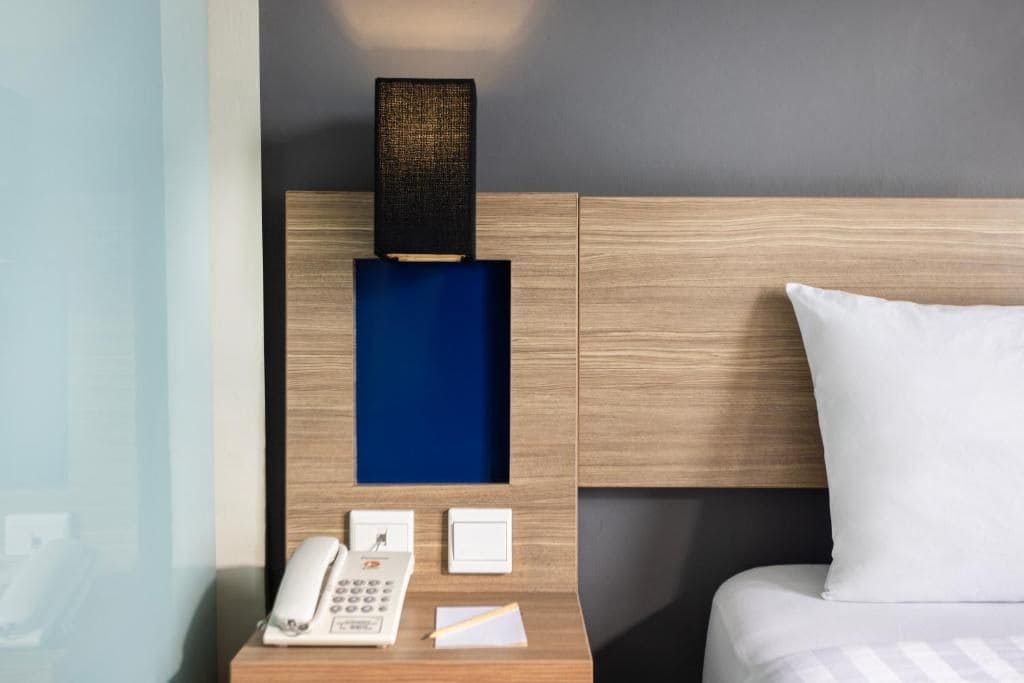 A hotel room with a wooden headboard, a bedside table with a telephone, a notepad, and a pen.