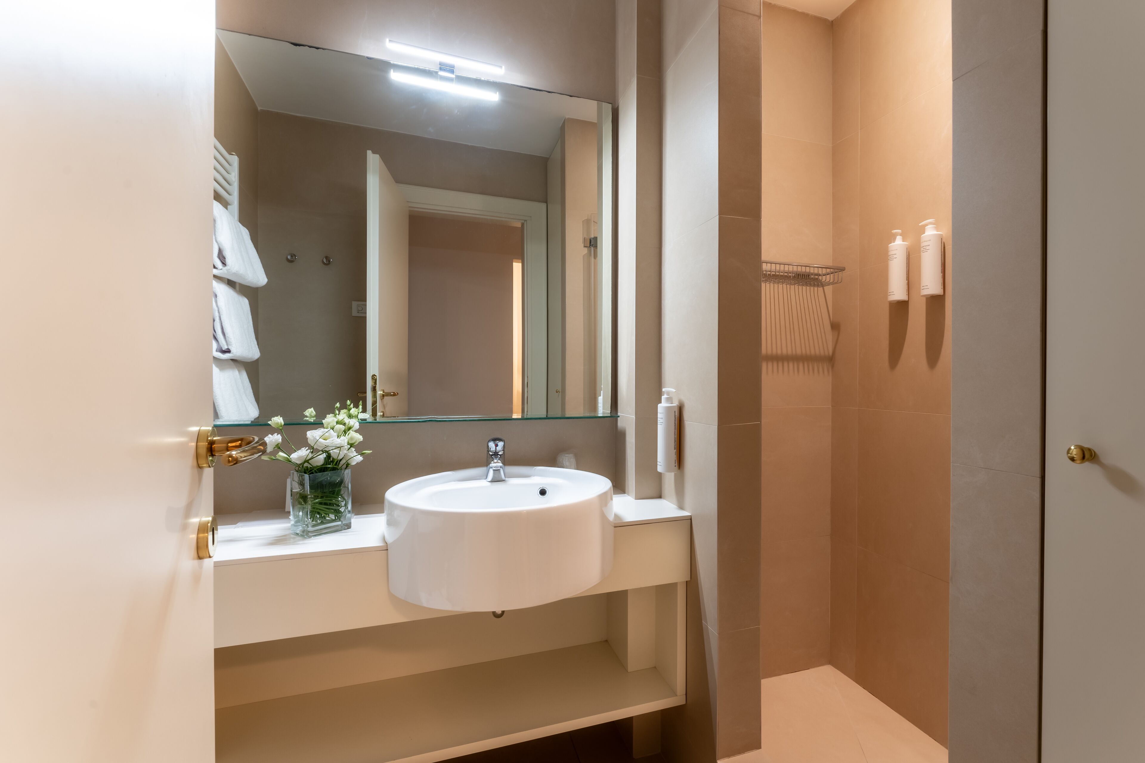 A modern bathroom with a white sink, a glass vase with flowers, a mirror, and a towel rack.