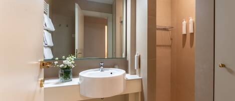 A modern bathroom with a white sink, a glass vase with flowers, a mirror, and a towel rack.