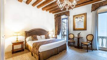 Une chambre avec un grand lit, des poutres apparentes en bois au plafond, un lustre, une petite table avec des chaises et une vue sur un balcon.