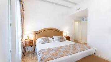 Un dormitorio con una cama grande, dos mesitas de noche con lámparas, un cabecero de madera y un banco al pie de la cama.