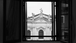 Vista a través de una ventana abierta de un edificio de arquitectura clásica, con estatuas y un reloj.