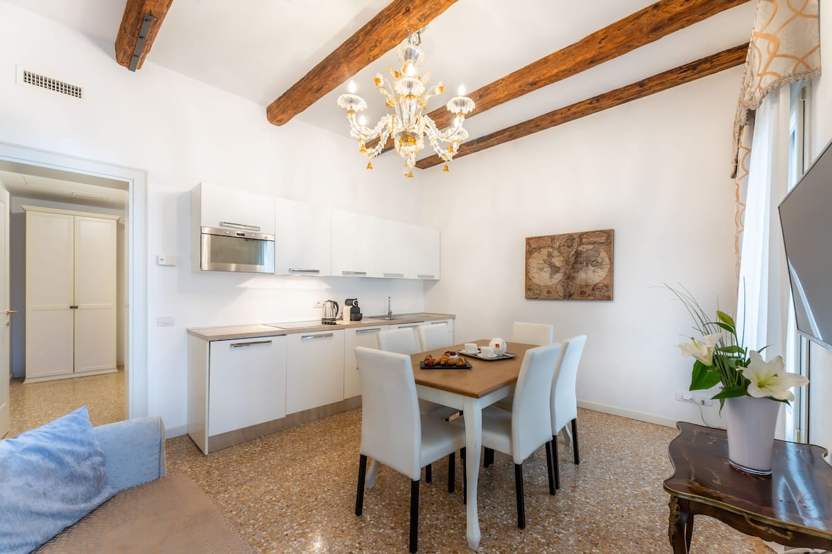 Een moderne keuken met witte kasten, een inbouwoven en een eethoek met een houten tafel en witte stoelen.