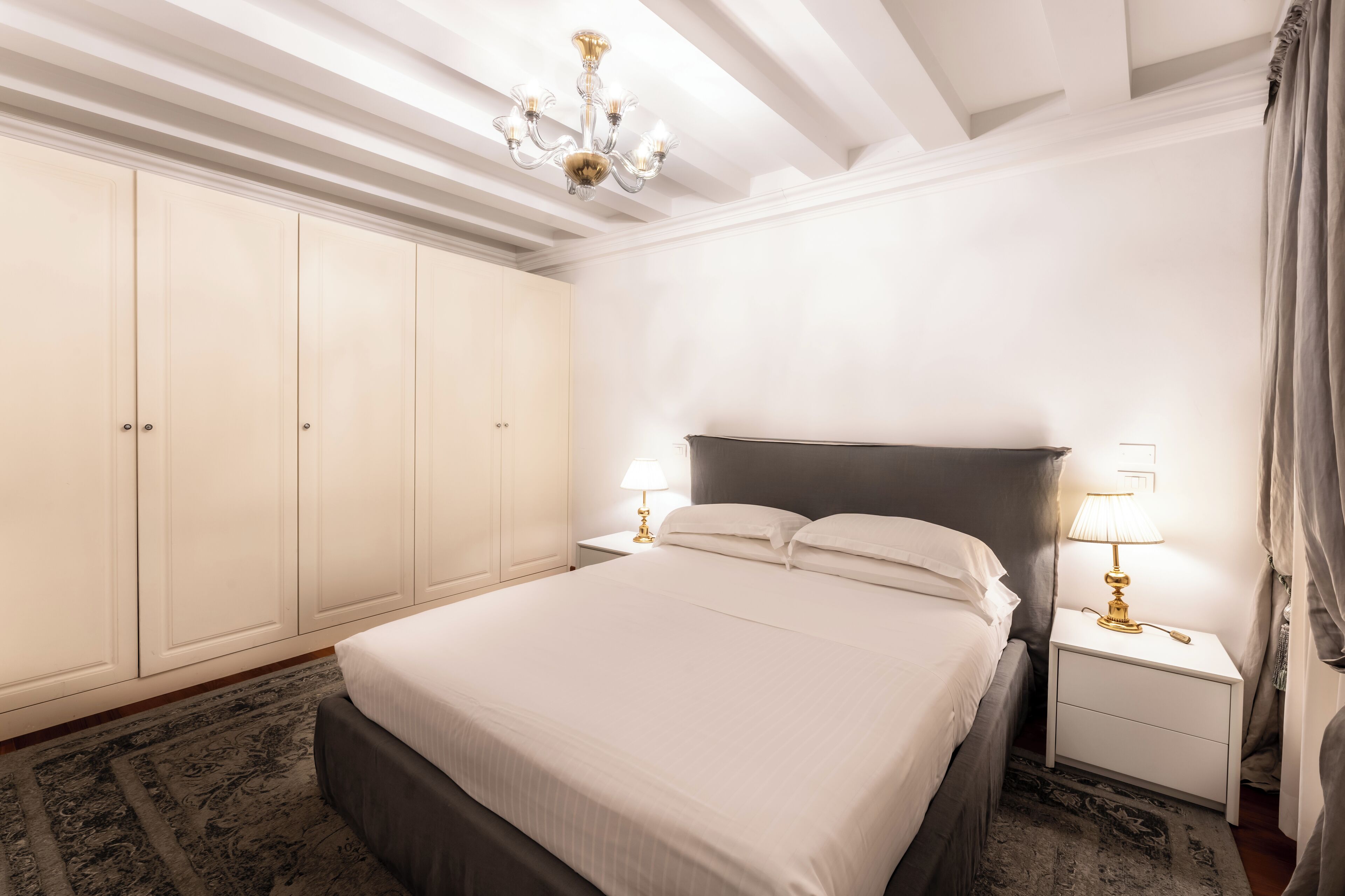 Een slaapkamer met een groot bed, twee nachtkastjes met lampen, een kledingkast en een kroonluchter.