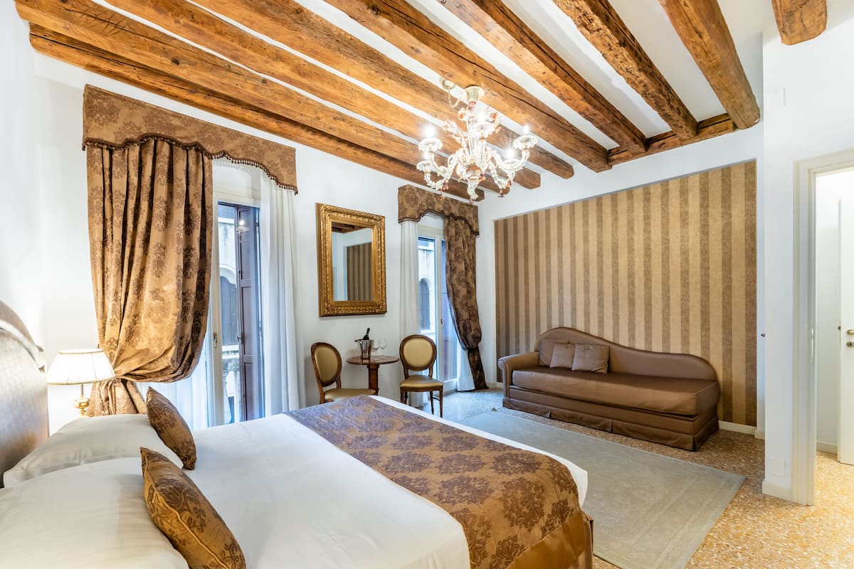 Een hotelkamer met een groot bed, een bank, een kroonluchter en uitzicht op de omgeving.