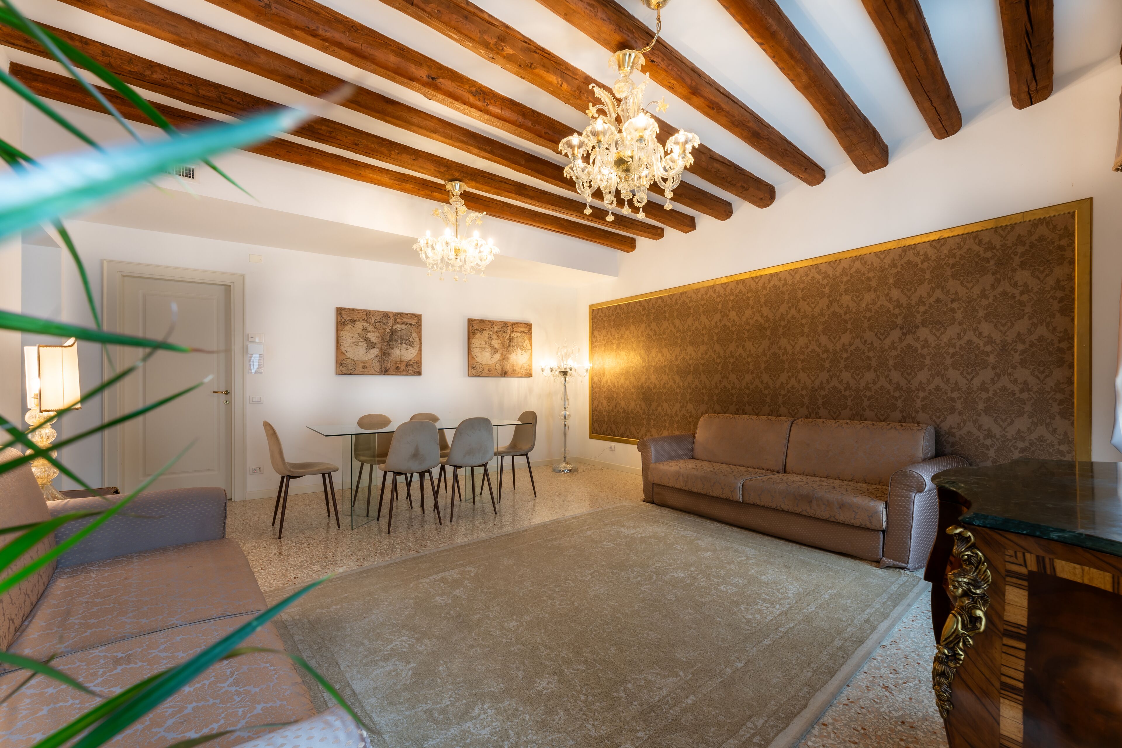A living room with a sofa, a dining table with chairs, a chandelier, and a patterned wall.