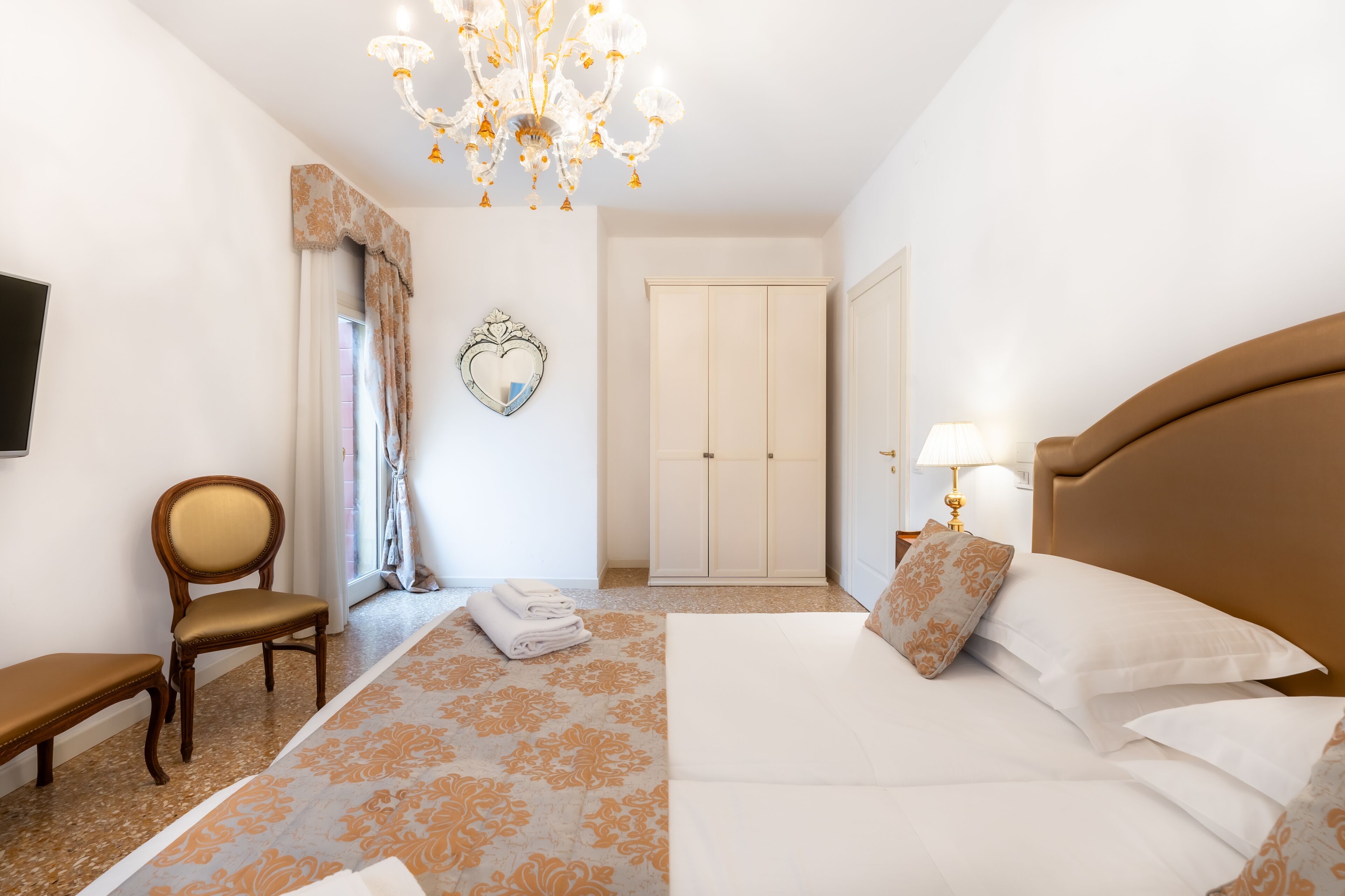 A hotel room with a bed, a chair, a wardrobe, and a chandelier.
