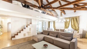 Una sala de estar moderna con un sofá seccional, una escalera de cristal y vigas de madera a la vista.