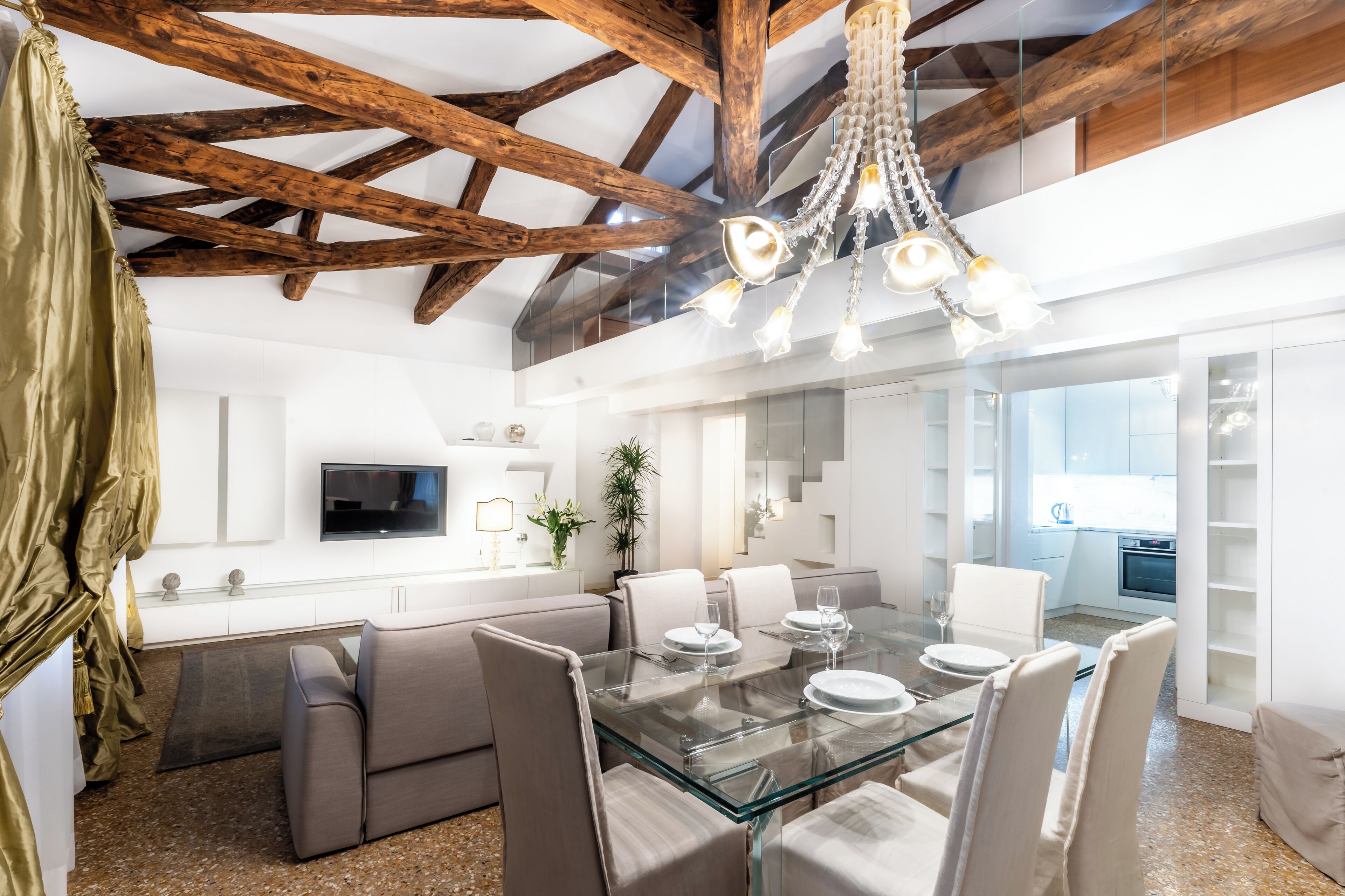 A modern dining area with a glass table, white chairs, and a chandelier.