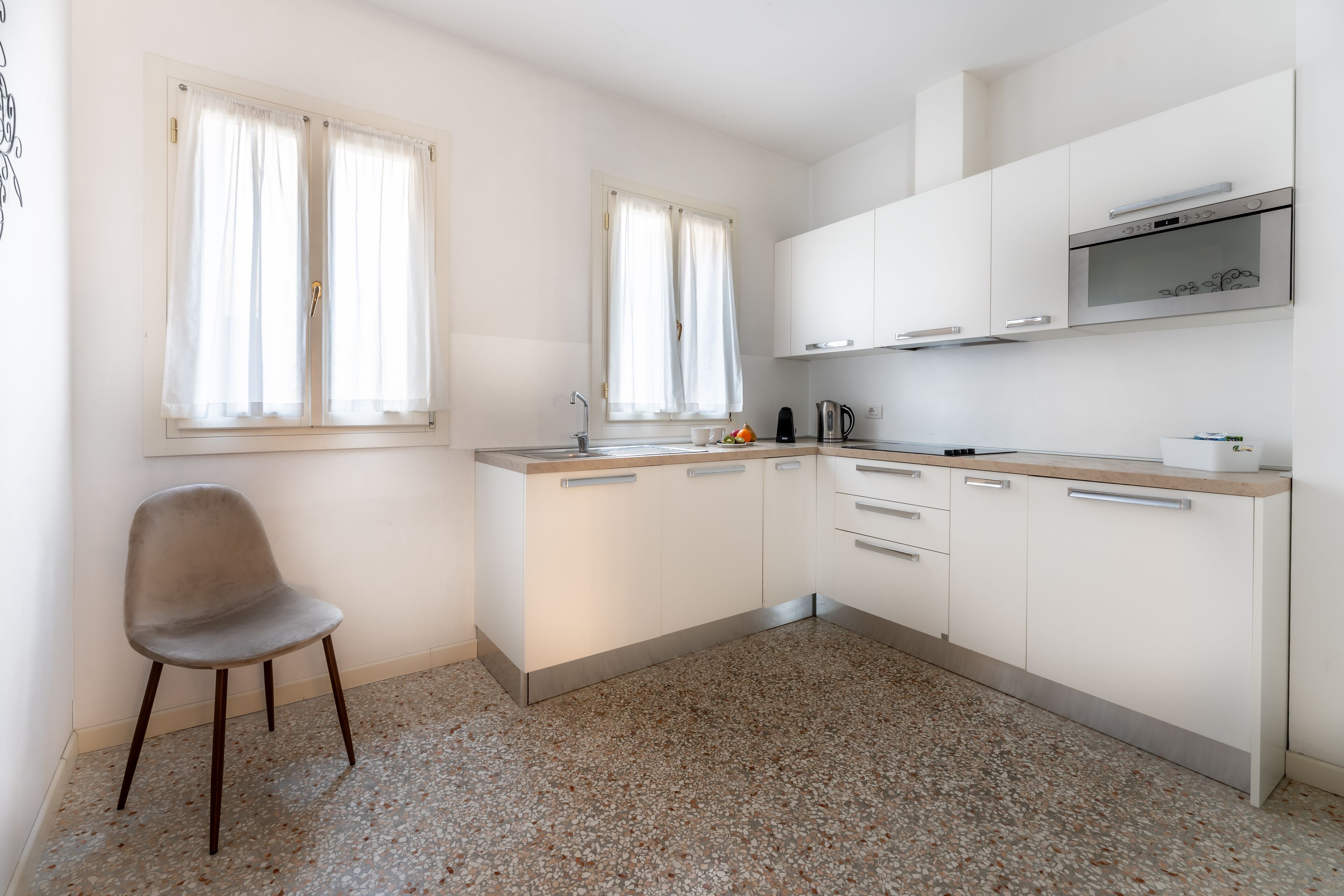 Una cocina moderna con armarios blancos, encimera de granito y una sola silla.